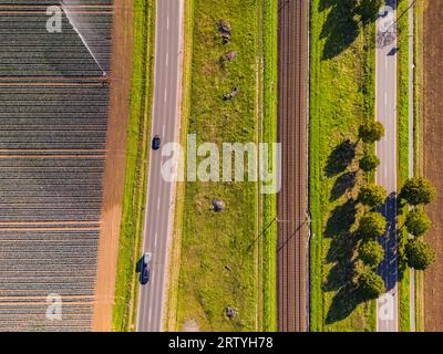 Una linea ferroviaria con due binari accanto a due strade e campi accanto ai campi agricoli Foto Stock
