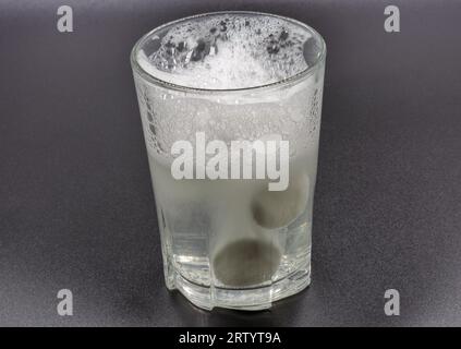 Sciogliendo le compresse effervescenti istantanee in un bicchiere d'acqua, il closeup è di colore nero Foto Stock