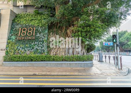 Cartello e albero all'angolo della strada che pubblicizza il 1881 Heritage Luxury Shopping plaza in una giornata di sole a Tsim Sha Tsui. Hong Kong Foto Stock