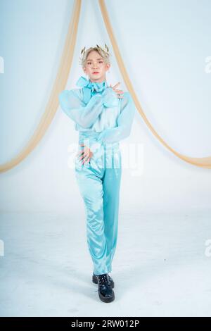 Una donna asiatica che posa elegantemente in un costume blu in una camera bianca Foto Stock