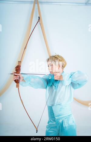 Una donna asiatica con i capelli biondi che tiene una freccia mentre indossa un vestito blu in una stanza bianca Foto Stock