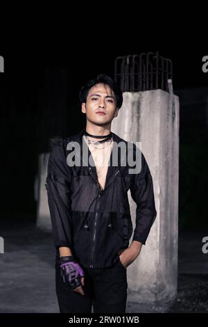 Un uomo asiatico vestito tutto con capelli neri e neri che si posa da uomo davanti a un pilastro dell'edificio Foto Stock