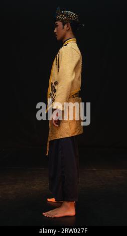 Un uomo asiatico che indossa un costume tradizionale con bellissimi motivi sulla camicia e indossa una bandana chiamata bendo in una stanza con sfondo nero Foto Stock