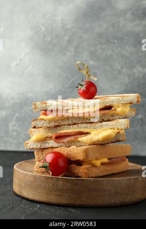 Pila di gustosi panini con prosciutto e formaggio fuso serviti con pomodori su tavola ruvida nera Foto Stock