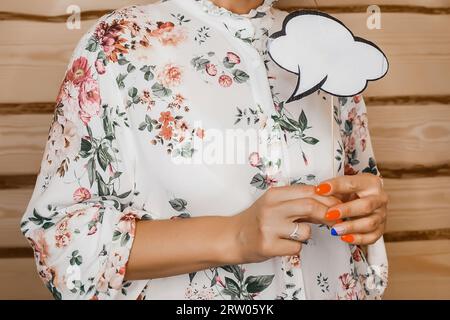 Una donna con un abito bianco con un motivo di fiori tiene tra le mani una manicure, uno spazio vuoto per pensieri e design vuoto su backgrou di legno Foto Stock