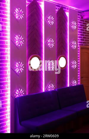Elemento decorativo di design interno con parete in mattoni, specchi, divano e luce rosa al neon. Foto Stock