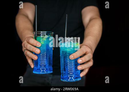 Le mani del barista servono 2 cocktail alcolici con sciroppo blu laguna blu su sfondo nero. Foto Stock