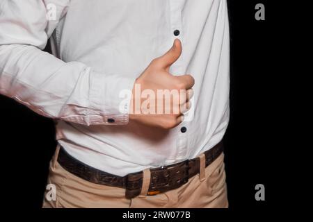 La mano di un ragazzo con una camicia bianca e pantaloni mostra la classe con i pollici su uno sfondo scuro. Foto Stock