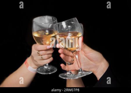 Due ragazze che bevono bicchieri con una bevanda alcolica, vino bianco, atmosfera di vacanza, riposo su sfondo nero, primo piano. Foto Stock