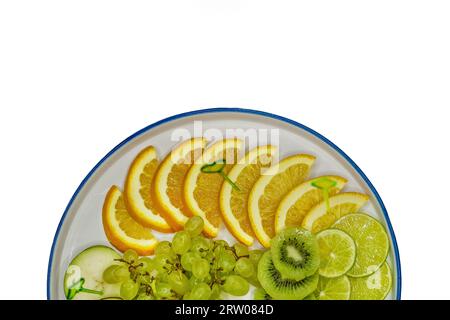 Piatto di frutta con uva, kiwi, lime, pera e arancia, a fette su fondo bianco, isolato. Foto Stock