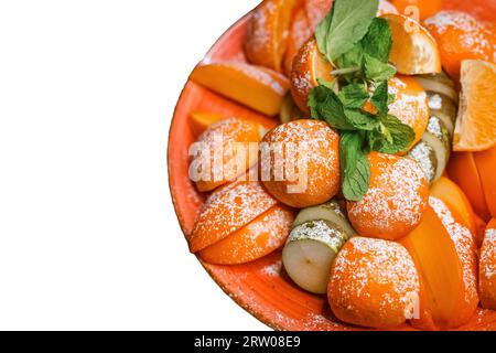 Piatto di frutta con mandarino, pera, cachi e guarnito con foglie di menta e cosparso di zucchero in polvere sullo sfondo bianco isolato. Foto Stock