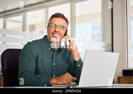 Sorridente uomo d'affari anziano che chiama al cellulare che lavora in ufficio. Foto Stock