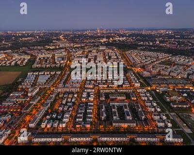 Le luci degli edifici e dei lampioni nel quartiere Riedberg di Francoforte brillano di sera, mentre lo skyline della banca si innalza sullo sfondo. Foto Stock