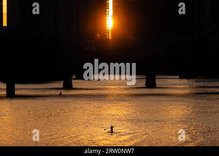 Alcuni rematori stand-up pagano sul meno a Francoforte poco di fronte al tramonto, mentre il sole splende un'ultima volta tra i grattacieli del Foto Stock