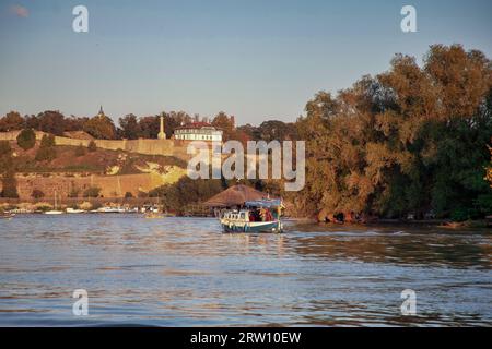 Belgrado, Serbia - Una barca a motore che naviga lungo il Danubio si avvicina al parco Kalemegdan e alla cittadella al tramonto Foto Stock