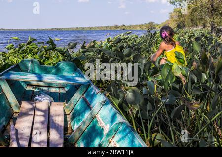 Puerto pollo, Paraguay l'8 agosto 2015: Una ragazza indigena seduta accanto a una piccola barca di pescatori a Puerto pollo a Rio Paraguay in Paraguay Foto Stock