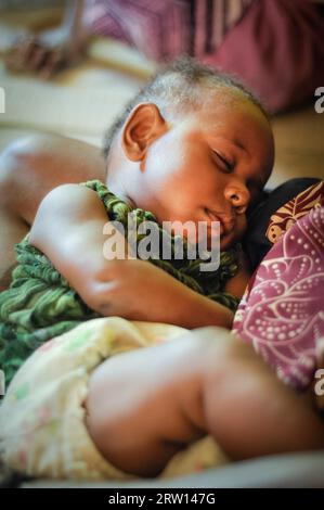 Palembe, Papua nuova Guinea, luglio 2015: Piccolo bambino addormentato in armi di sua madre a Palembe, fiume Sepik, Papua nuova Guinea. Documentario editoriale Foto Stock