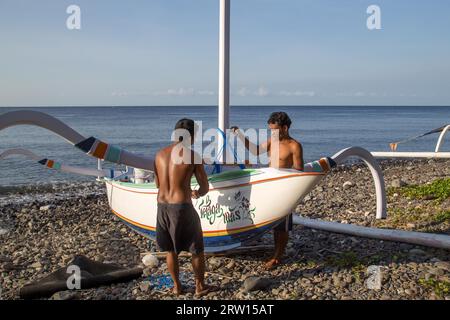 Bali, Indonesia, 6 luglio 2015: Due pescatori preparano le loro tradizionali barche da pesca su una spiaggia vicino ad Amed Foto Stock