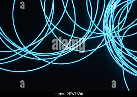 Uno sfondo insolito, unico e luminoso di cavi sottili impilati in modo caotico, celeste, blu, azzurro, imbracatura al neon, filo illuminato, filo sottile posizionato Foto Stock