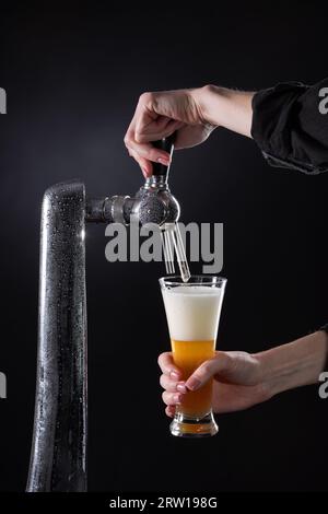 Il barista versa birra fresca dal rubinetto in un bicchiere su sfondo scuro. Foto di alta qualità Foto Stock