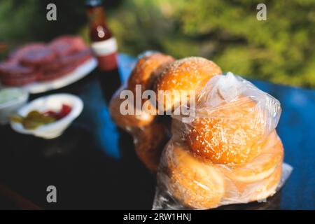 Processo di cottura e grigliatura degli hamburger di manzo durante il festival all'aperto del cibo di strada, vista delle mani dello chef nei guanti con una varietà di ingredienti su un grill Foto Stock