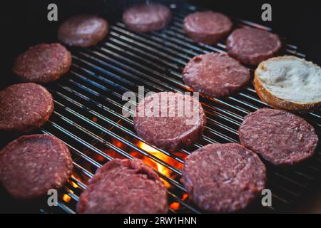 Processo di cottura e grigliatura degli hamburger di manzo durante il festival all'aperto del cibo di strada, vista delle mani dello chef nei guanti con una varietà di ingredienti su un grill Foto Stock