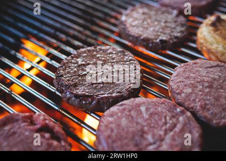 Processo di cottura e grigliatura degli hamburger di manzo durante il festival all'aperto del cibo di strada, vista delle mani dello chef nei guanti con una varietà di ingredienti su un grill Foto Stock