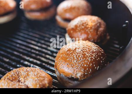 Processo di cottura e grigliatura degli hamburger di manzo durante il festival all'aperto del cibo di strada, vista delle mani dello chef nei guanti con una varietà di ingredienti su un grill Foto Stock