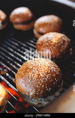 Processo di cottura e grigliatura degli hamburger di manzo durante il festival all'aperto del cibo di strada, vista delle mani dello chef nei guanti con una varietà di ingredienti su un grill Foto Stock