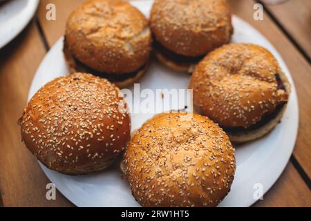 Processo di cottura e grigliatura degli hamburger di manzo durante il festival all'aperto del cibo di strada, vista delle mani dello chef nei guanti con una varietà di ingredienti su un grill Foto Stock