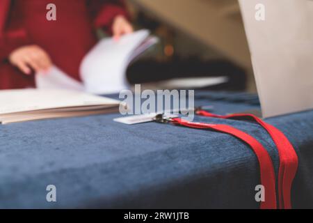 Processo di check-in su un evento del forum congressuale, tavolo della reception di registrazione, visitatori e partecipanti che ricevono il badge con il nome e i wri d'ingresso Foto Stock