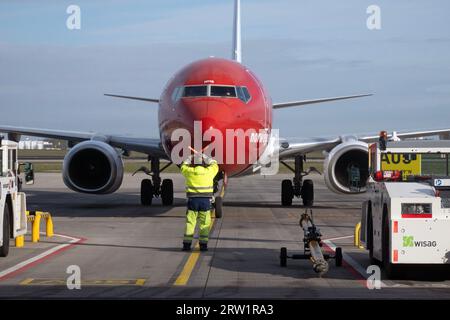 31.03.2023, Germania, Brandeburgo, Schoenefeld - controllore di terra che dirige un aeromobile Norwegian Airlines verso la sua posizione di parcheggio sul piazzale di BER Foto Stock