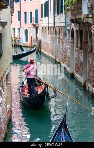 Vista panoramica di un canale a Venezia, Italia, con gondola e iconico gondoliere a righe rosse, Venezia, Foto Stock