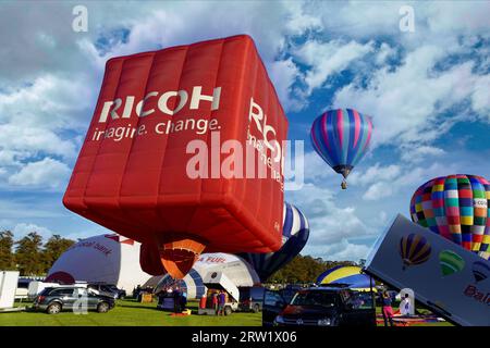 Grande mongolfiera Ricoh rossa a forma di cubo che si prepara a decollare con un pallone in lontananza, York Balloon Fiesta, North Yorkshire, Regno Unito. Foto Stock