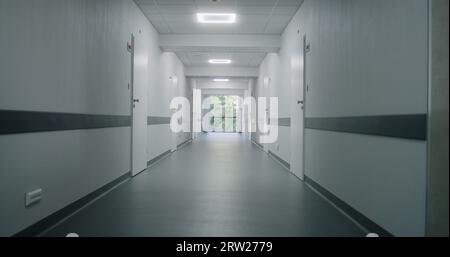 Moderno centro medico con corridoio vuoto prima di iniziare il lavoro. Corridoi ospedalieri e porte di armadietti illuminati da lampade a LED. Sistema sanitario. Clinica chiusa in quarantena. Pandemia. Foto Stock
