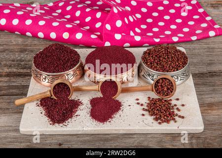 Asciugare il sumac delle spezie in un cucchiaio di legno. Spezie sumac in polvere. Spezie in polvere di Sumac rosso macinato essiccato in cucchiaio di legno con bacche di sumac su tavola rustica. Salute Foto Stock