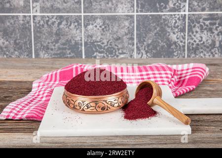 Asciugare il sumac delle spezie in un cucchiaio di legno. Spezie sumac in polvere. Spezie in polvere di Sumac rosso macinato essiccato in cucchiaio di legno con bacche di sumac su tavola rustica. Salute Foto Stock