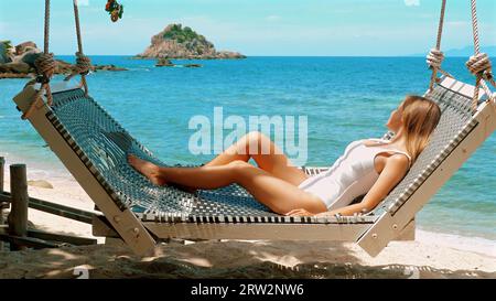 Donna che si rilassa sull'amaca della spiaggia con vista mare Foto Stock