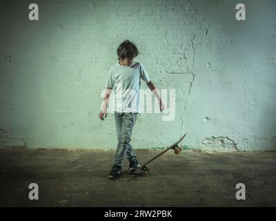 Ragazzo che pratica lo skateboard davanti a un vecchio muro di mattoni bianchi. Foto Stock