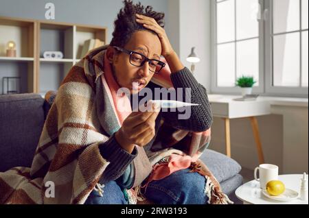 Un giovane seduto con il termometro si sente male Foto Stock