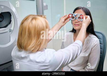 Optometrista che esegue la rifrazione soggettiva binoculare su una paziente di sesso femminile Foto Stock