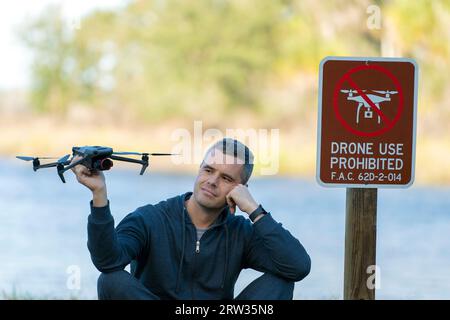 L'uomo volerà il suo quadricottero in nessuna zona di droni. L'operatore utilizza illegalmente il proprio UAS nel parco statale vicino al segnale di restrizione Foto Stock