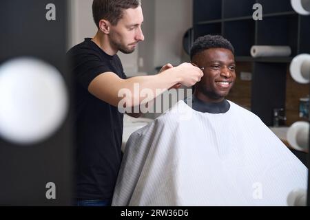 Il parrucchiere taglia i capelli dei clienti davanti allo specchio nel barbiere Foto Stock