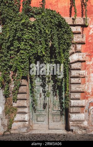 Verde verde edera su un'antica porta rustica di un edificio residenziale nel colorato e storico quartiere di Trastevere a Roma, Italia. Foto Stock