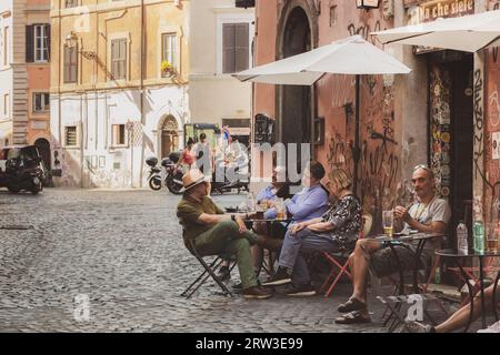 Roma, Italia - 27 agosto 2023: I clienti locali in un pomeriggio soleggiato si siedono all'aperto in un caffè di strada con bevande nello storico Rione vi Parione distri Foto Stock