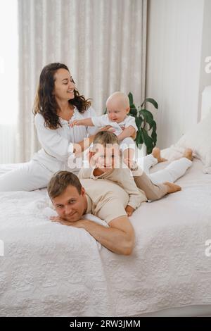 Famiglia con due bambini sul letto che si divertono. Mather, il padre, il bambino e i bambini piccoli sono felici la mattina in camera da letto. Bambini che giocano con i genitori al Foto Stock