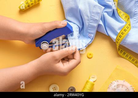 Mani femminili con forniture diverse che cuciscono blusa su sfondo giallo Foto Stock