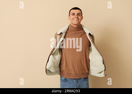 Giovane uomo con giacca in pelle di montone su sfondo beige Foto Stock