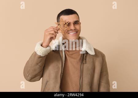 Giovane uomo con giacca in pelle di montone con fiocco di neve su sfondo beige Foto Stock