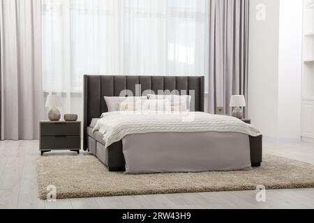 Elegante camera da letto dai colori tenui con comodo letto e comodino. Design degli interni Foto Stock